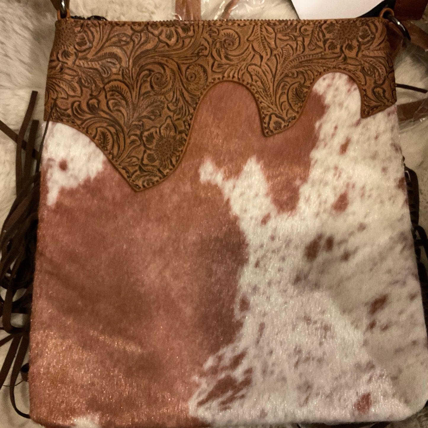 A brown and white cowhide crossbody bag with embossed leather details and fringes.